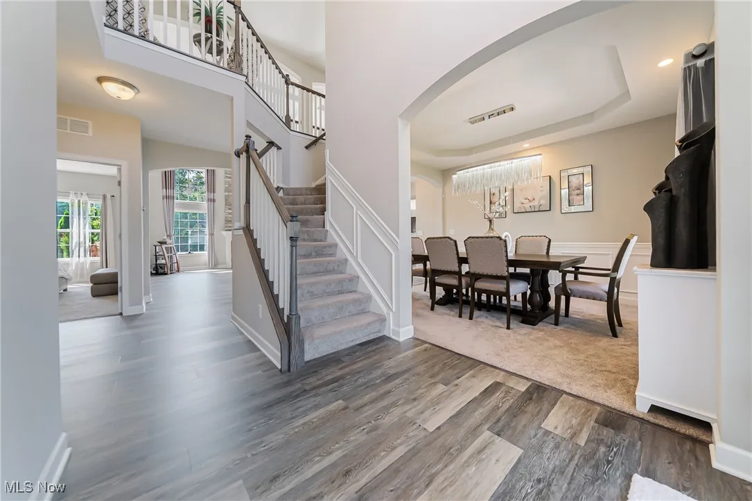 Foyer entrance with arched walkways, dark wood-style flooring, stairs, and a tray ceiling