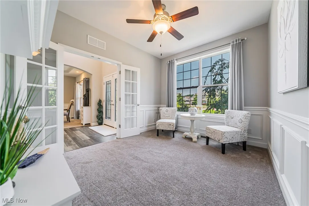 Living area featuring french doors, a decorative wall, arched walkways, wainscoting, and carpet