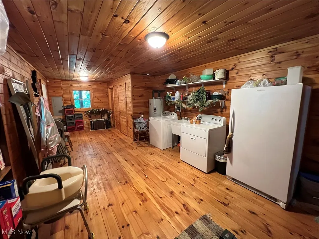 Laundry room with wooden walls, light wood-type flooring, independent washer and dryer, and wood ceiling