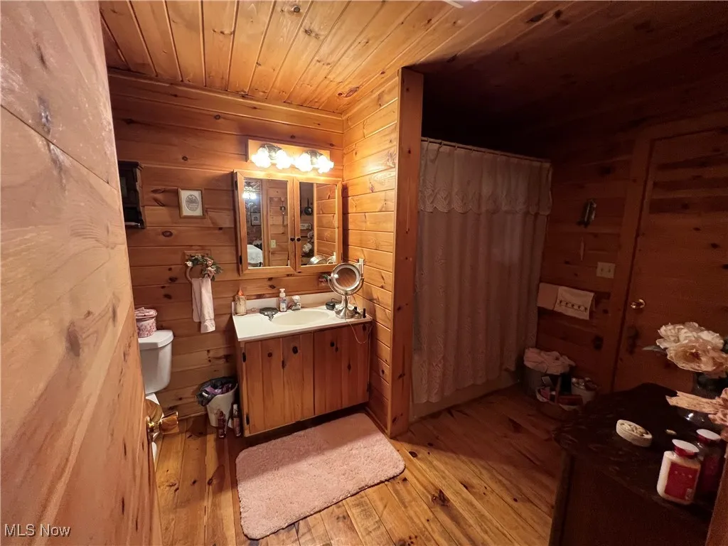 Full bathroom featuring wooden ceiling, wooden walls, hardwood / wood-style flooring, vanity, and a shower with shower curtain