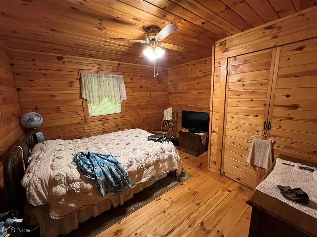Bedroom with light wood finished floors, wooden walls, and wood ceiling