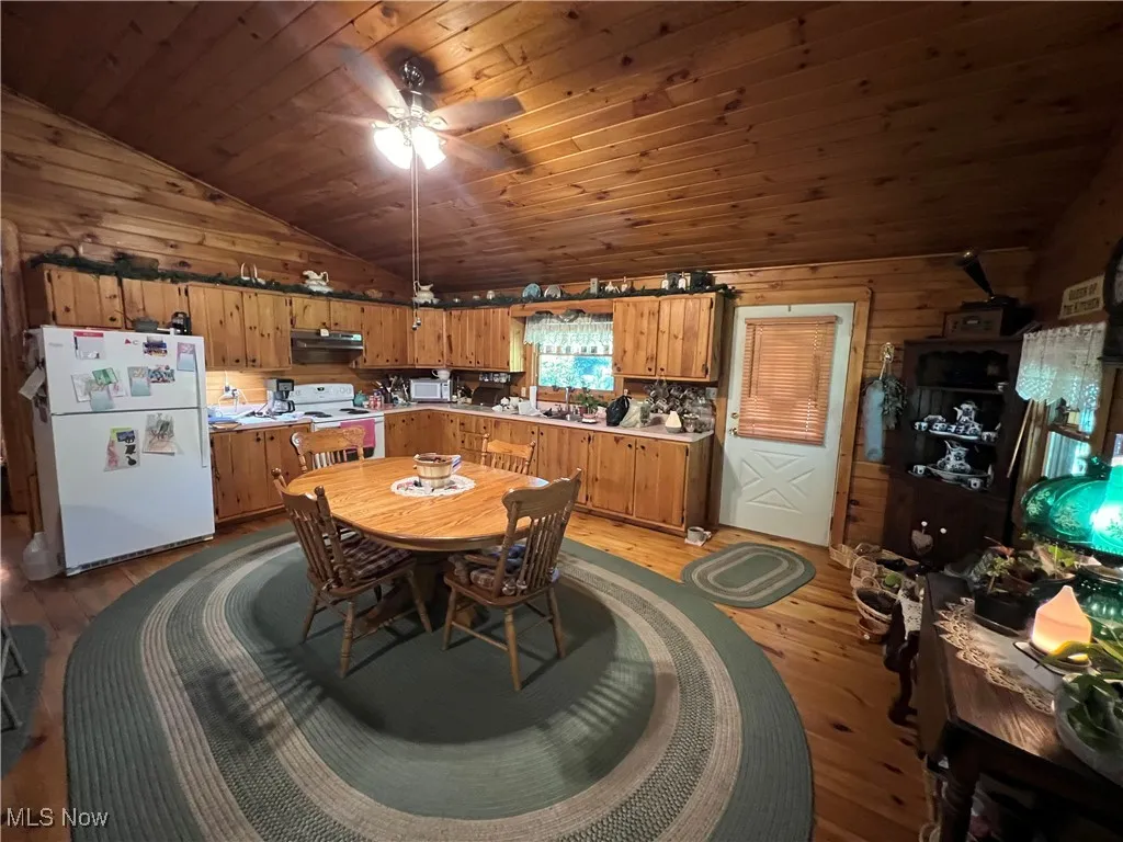 Kitchen featuring lofted ceiling, wooden walls, white appliances, light wood-type flooring, and brown cabinetry