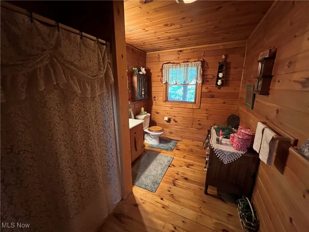 Bathroom with wood ceiling, hardwood / wood-style flooring, wooden walls, vanity, and curtained shower