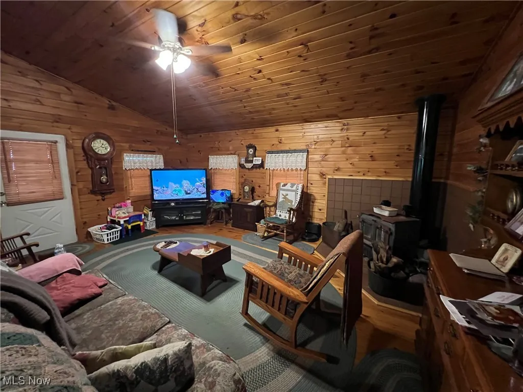 Living area featuring lofted ceiling, a ceiling fan, wood walls, a wood stove, and wood ceiling