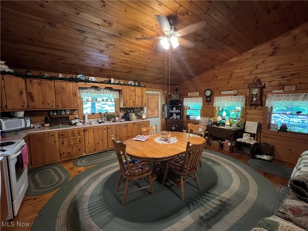Dining space with light wood-style floors, vaulted ceiling, wood walls, a ceiling fan, and wooden ceiling