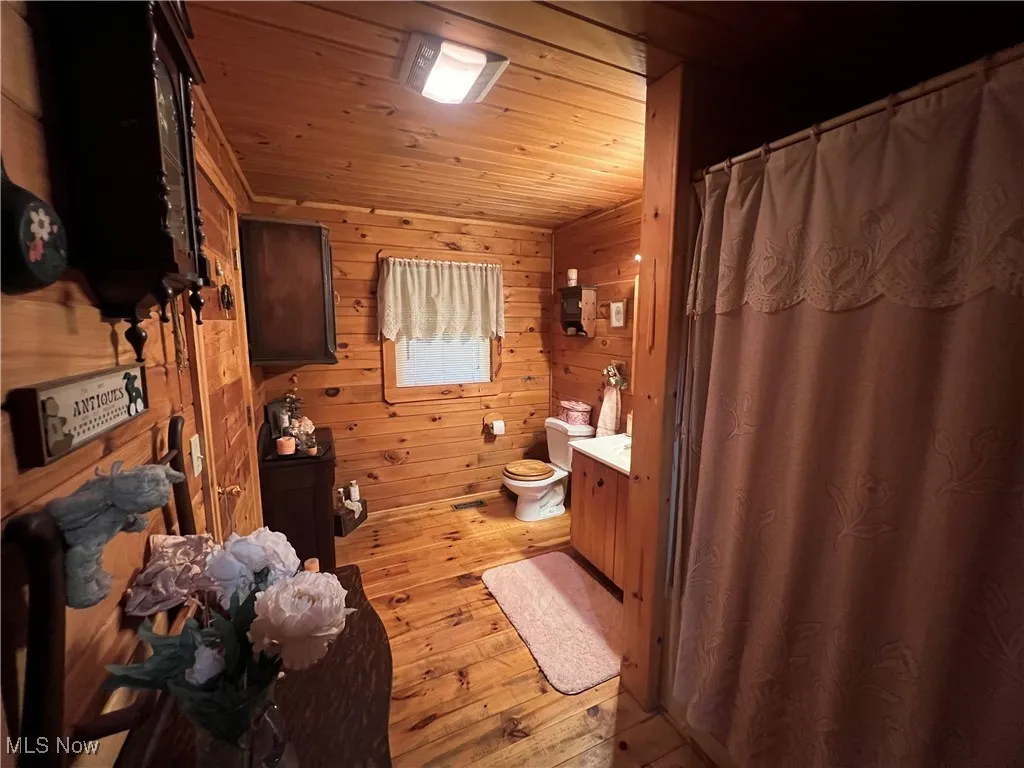 Full bath featuring hardwood / wood-style floors, wood walls, wood ceiling, a shower with curtain, and vanity