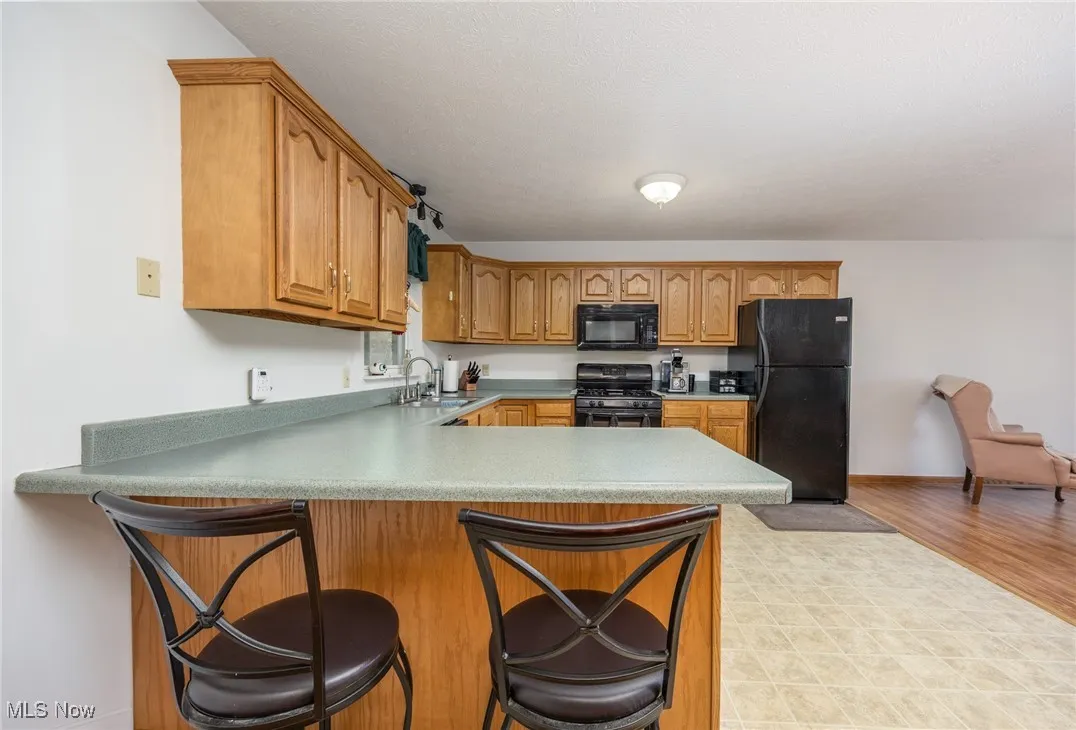 Kitchen with black appliances, brown cabinetry, a peninsula, a breakfast bar area, and light countertops