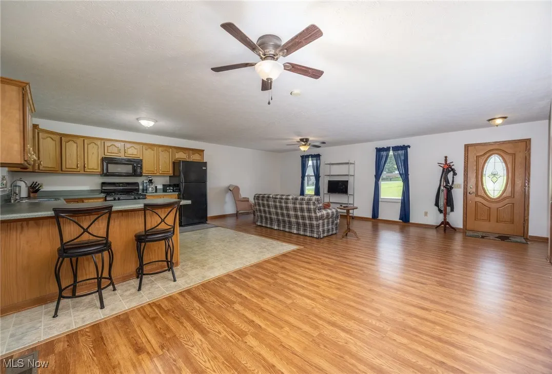 Kitchen with light wood finished floors, ceiling fan, a peninsula, open floor plan, and black appliances