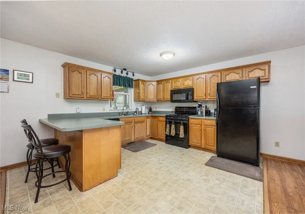Kitchen featuring black appliances, a peninsula, brown cabinets, a breakfast bar, and light floors