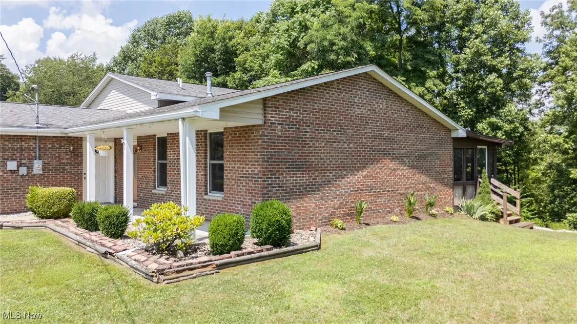 View of side of property featuring brick siding, a lawn, and a shingled roof