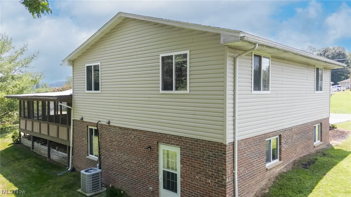View of side of home featuring a lawn, a sunroom, and brick siding