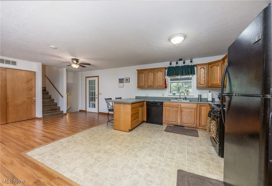 Kitchen featuring black appliances, a peninsula, a ceiling fan, brown cabinets, and open floor plan