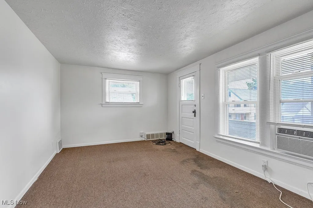 Carpeted spare room featuring a textured ceiling and baseboards