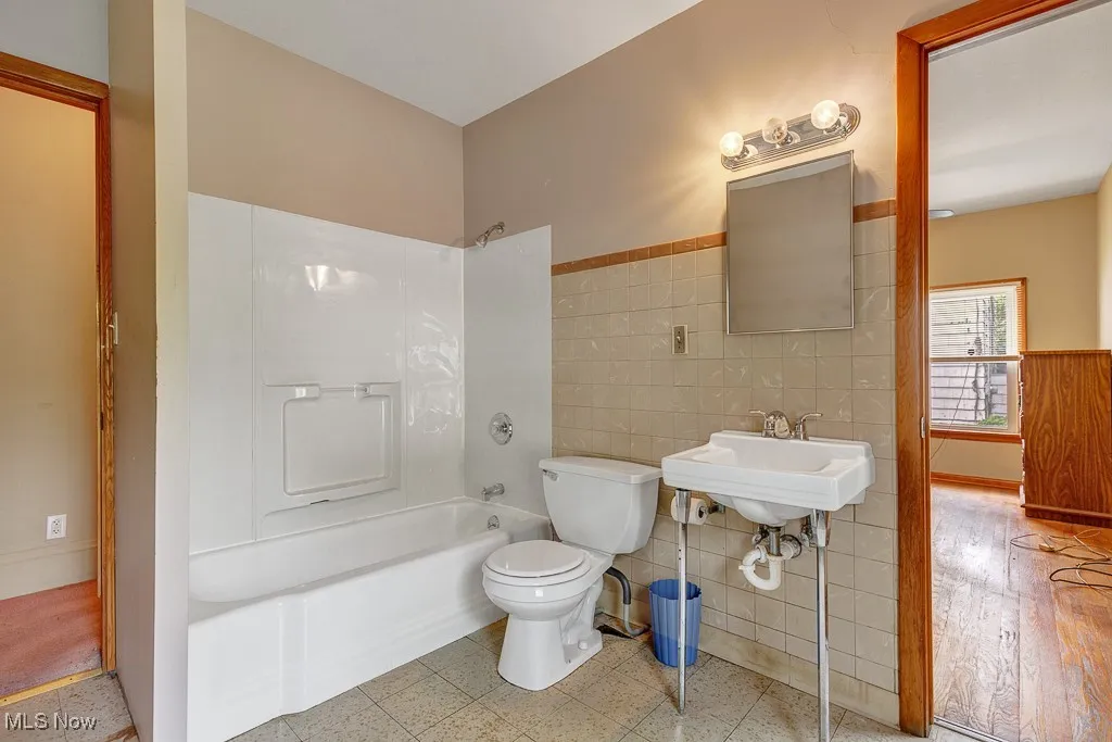 Bathroom with tile walls, washtub / shower combination, and wainscoting