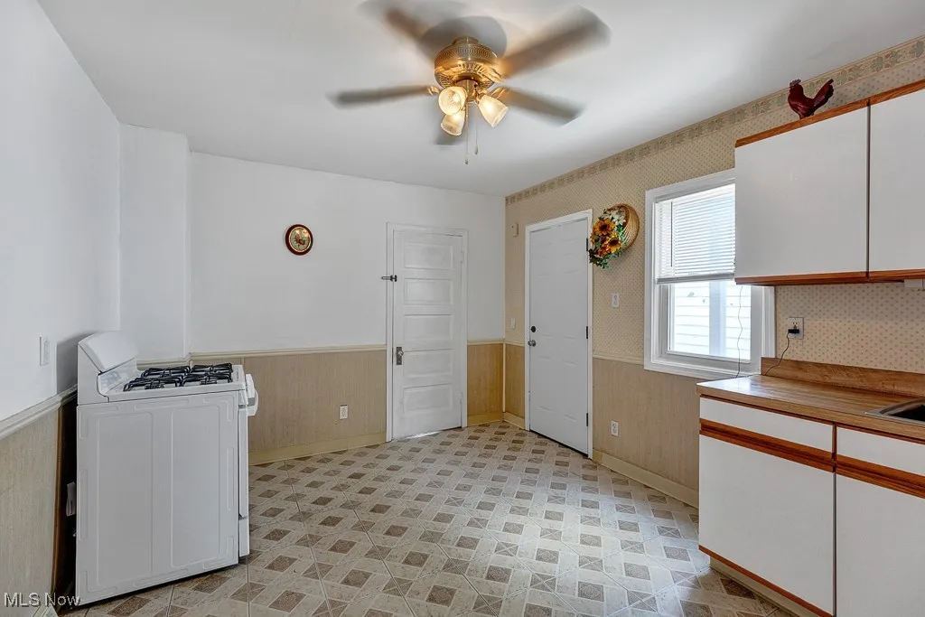 Kitchen featuring a wainscoted wall, a ceiling fan, white gas range oven, white cabinetry, and wooden walls