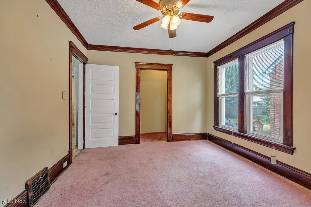 Unfurnished bedroom featuring carpet floors, crown molding, a textured ceiling, and a ceiling fan