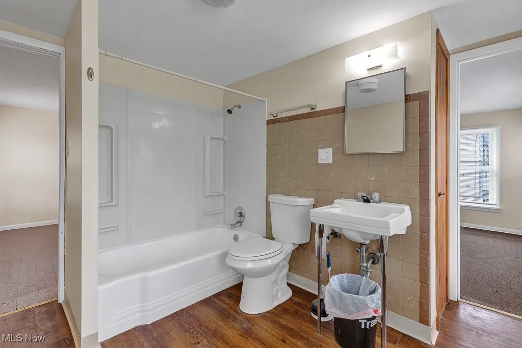 Full bathroom featuring tile walls,  shower combination, and wood finished floors