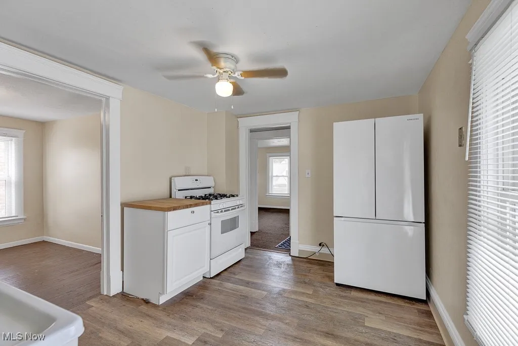 Kitchen featuring wooden counters, white appliances, light wood-style flooring, ceiling fan, and white cabinetry