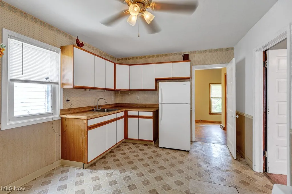 Kitchen featuring freestanding refrigerator, a ceiling fan, white cabinetry, light countertops, and wallpapered walls