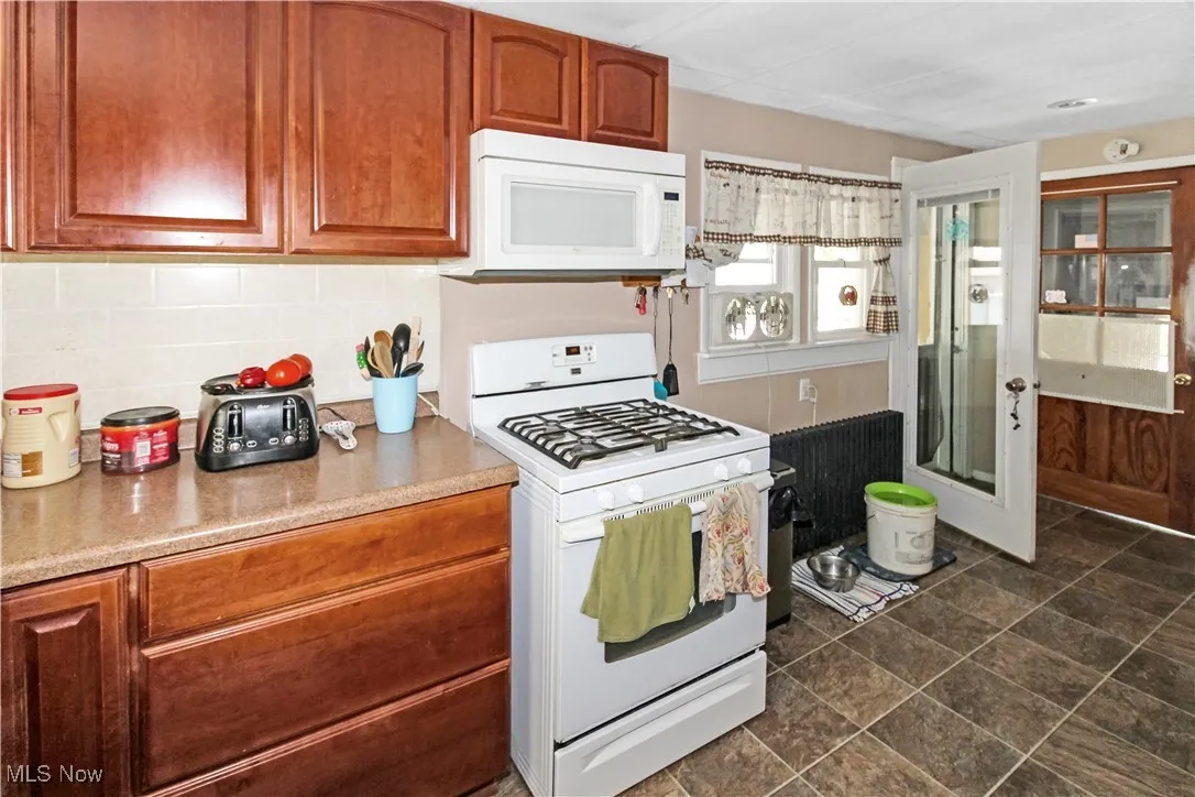 Kitchen featuring white appliances, decorative backsplash, and light countertops