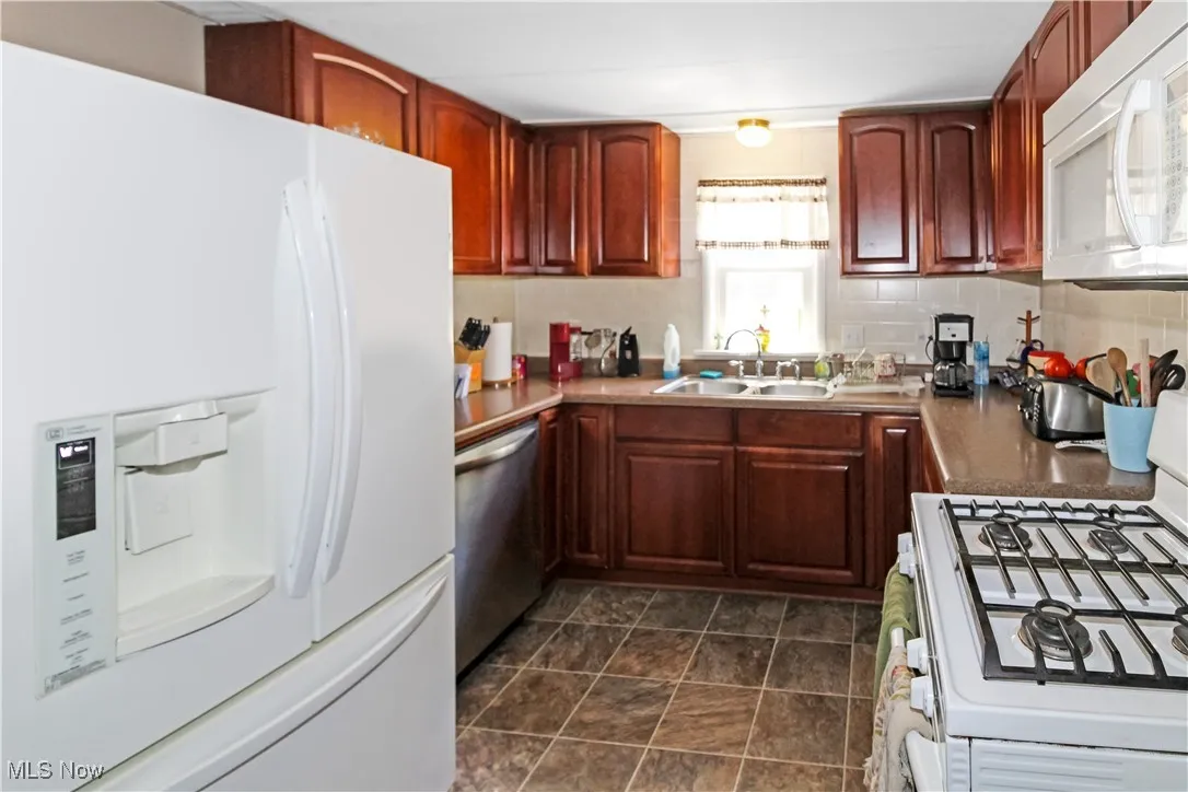 Kitchen featuring white appliances, tasteful backsplash, and reddish brown cabinets