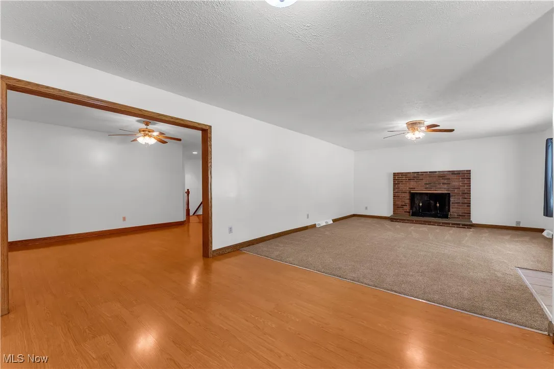 Unfurnished living room with ceiling fan, wood finished floors, a fireplace, and a textured ceiling
