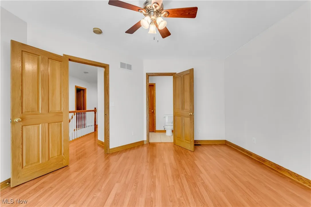 Unfurnished bedroom featuring light wood-style flooring, ceiling fan, and ensuite bath