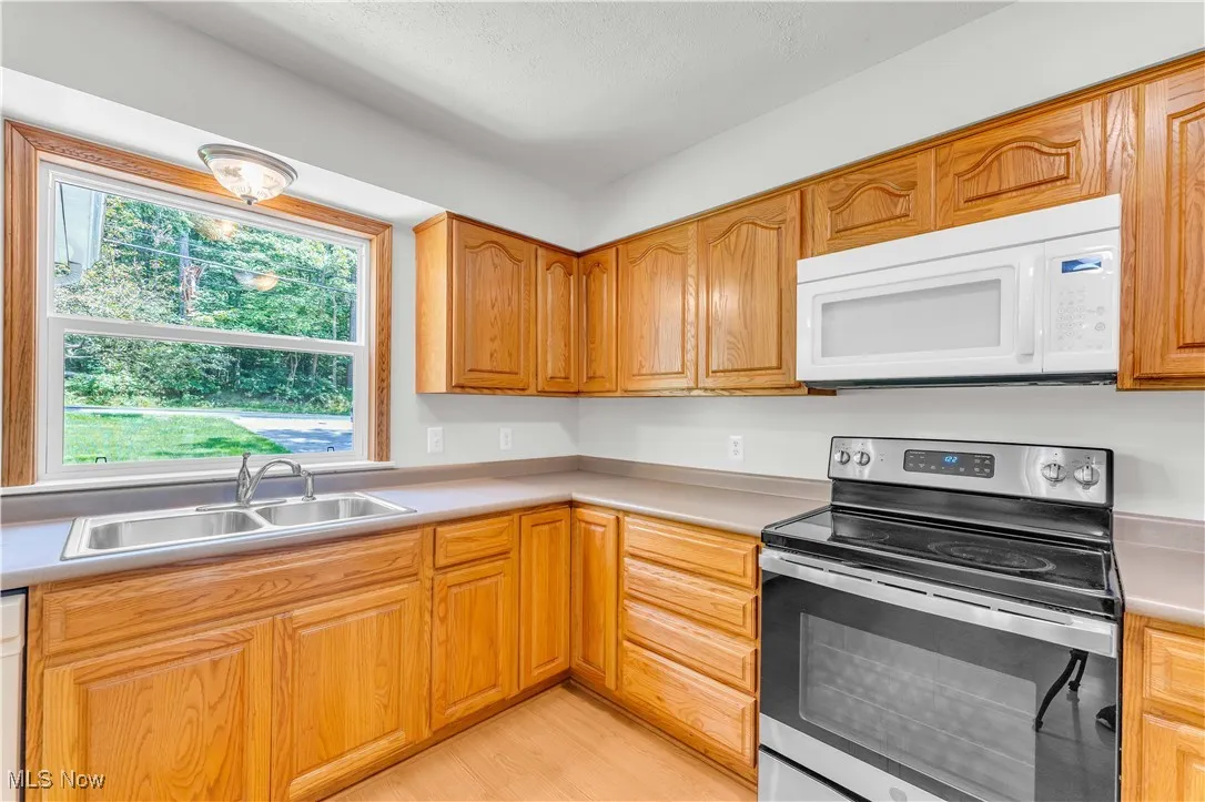 Kitchen featuring stainless steel range with electric stovetop, white microwave, light countertops, light wood-style floors, and brown cabinetry