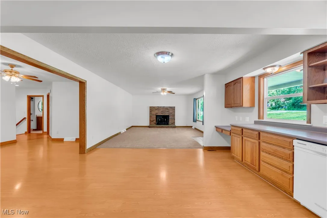 Kitchen with a ceiling fan, dishwasher, light wood-type flooring, a fireplace with raised hearth, and a textured ceiling