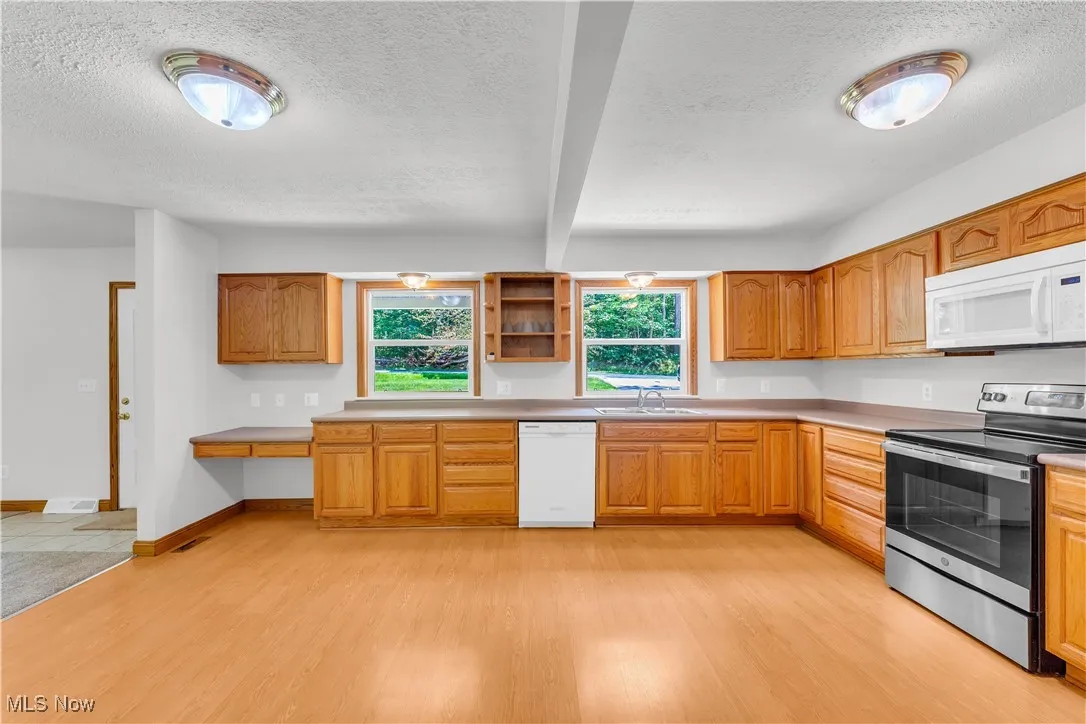 Kitchen featuring white appliances, light wood finished floors, a textured ceiling, and brown cabinets
