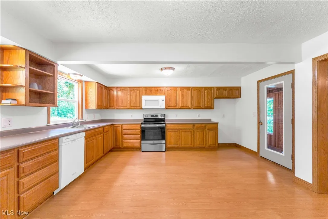 Kitchen with light wood-type flooring, white appliances, brown cabinets, a textured ceiling, and light countertops