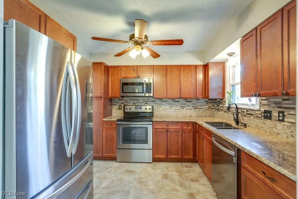 Kitchen featuring appliances with stainless steel finishes, ceiling fan, tasteful backsplash, and light stone countertops