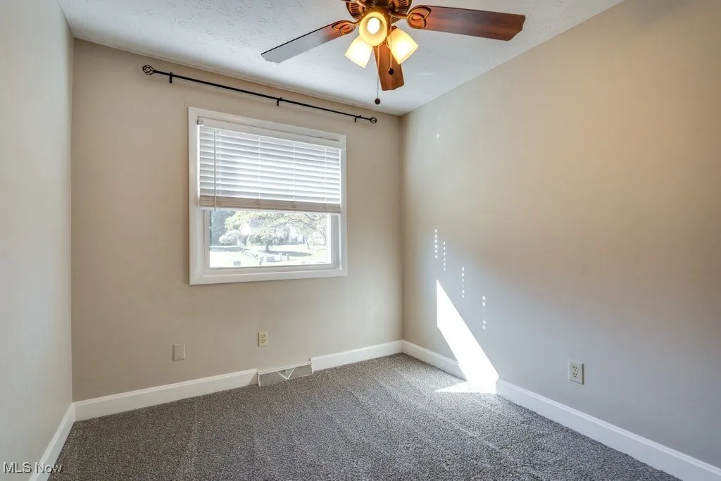 Carpeted empty room featuring a ceiling fan and baseboards