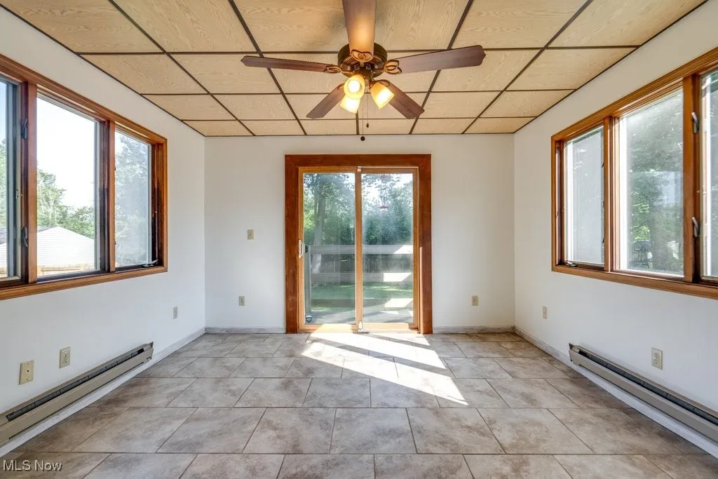 Unfurnished room featuring a baseboard heating unit, a ceiling fan, and light tile patterned floors