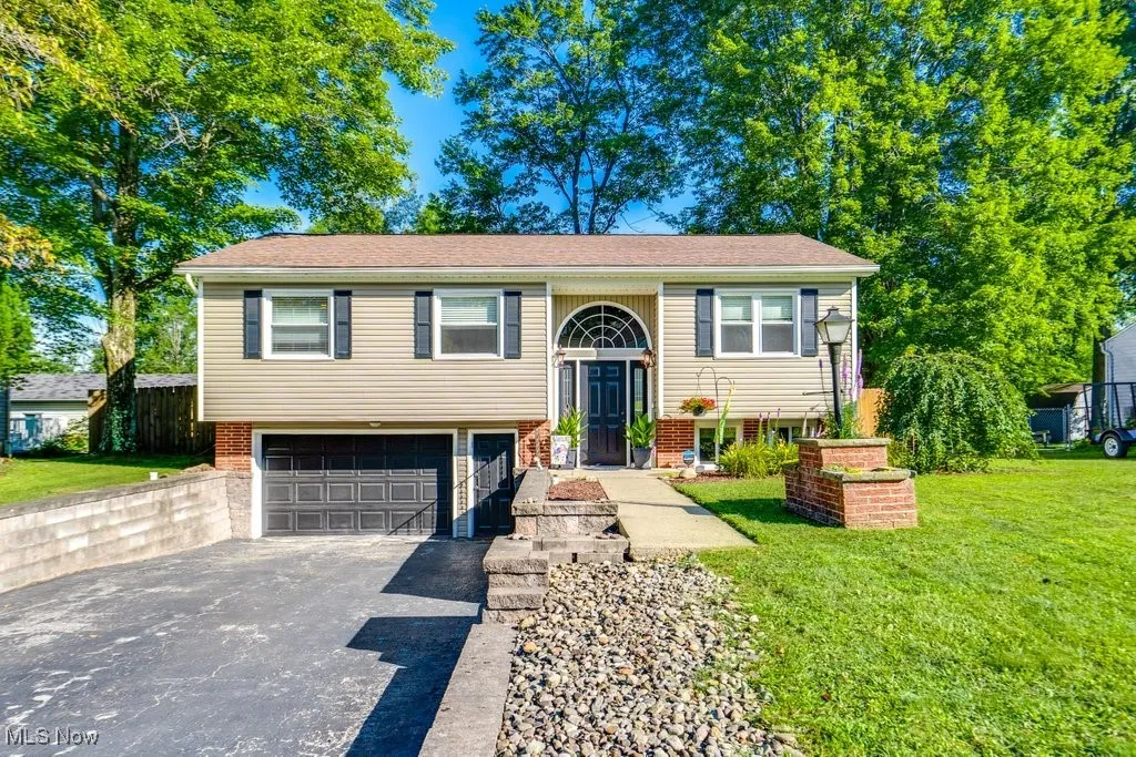 Split foyer home featuring driveway, brick siding, a garage, a front yard, and a shingled roof