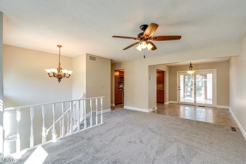Carpeted empty room featuring a chandelier, ceiling fan, and tile patterned floors