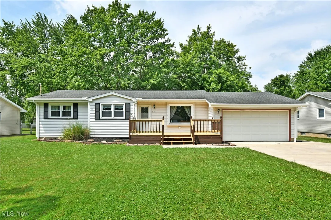 Ranch-style house with driveway, a garage, a front lawn, a wooden deck, and roof with shingles