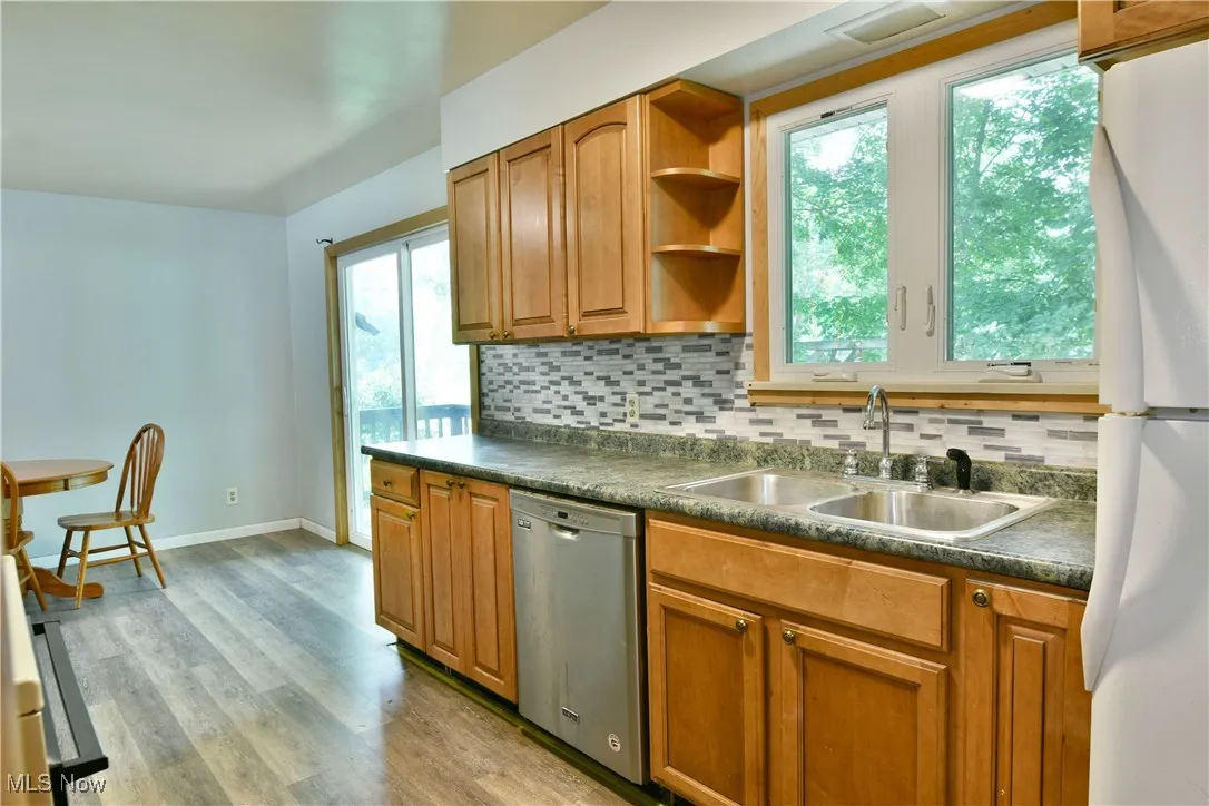 Kitchen featuring dishwasher, dark countertops, freestanding refrigerator, and backsplash