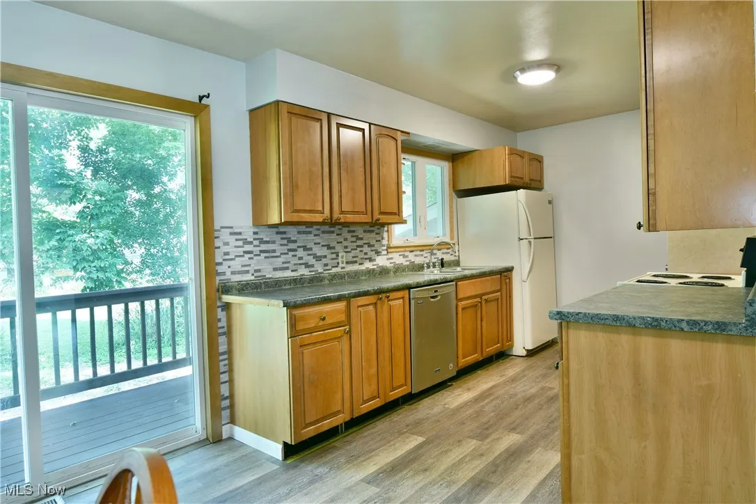 Kitchen with light wood-style flooring, backsplash, stainless steel dishwasher, and freestanding refrigerator