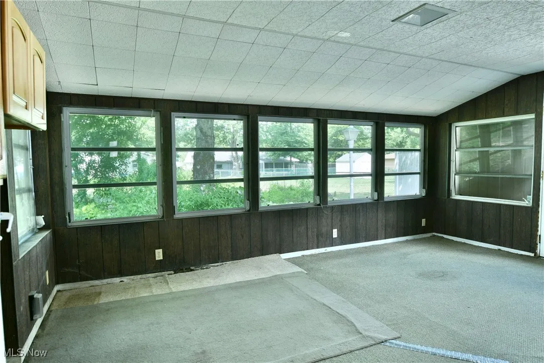 Unfurnished sunroom featuring carpet floors, wood walls, healthy amount of natural light, and vaulted ceiling