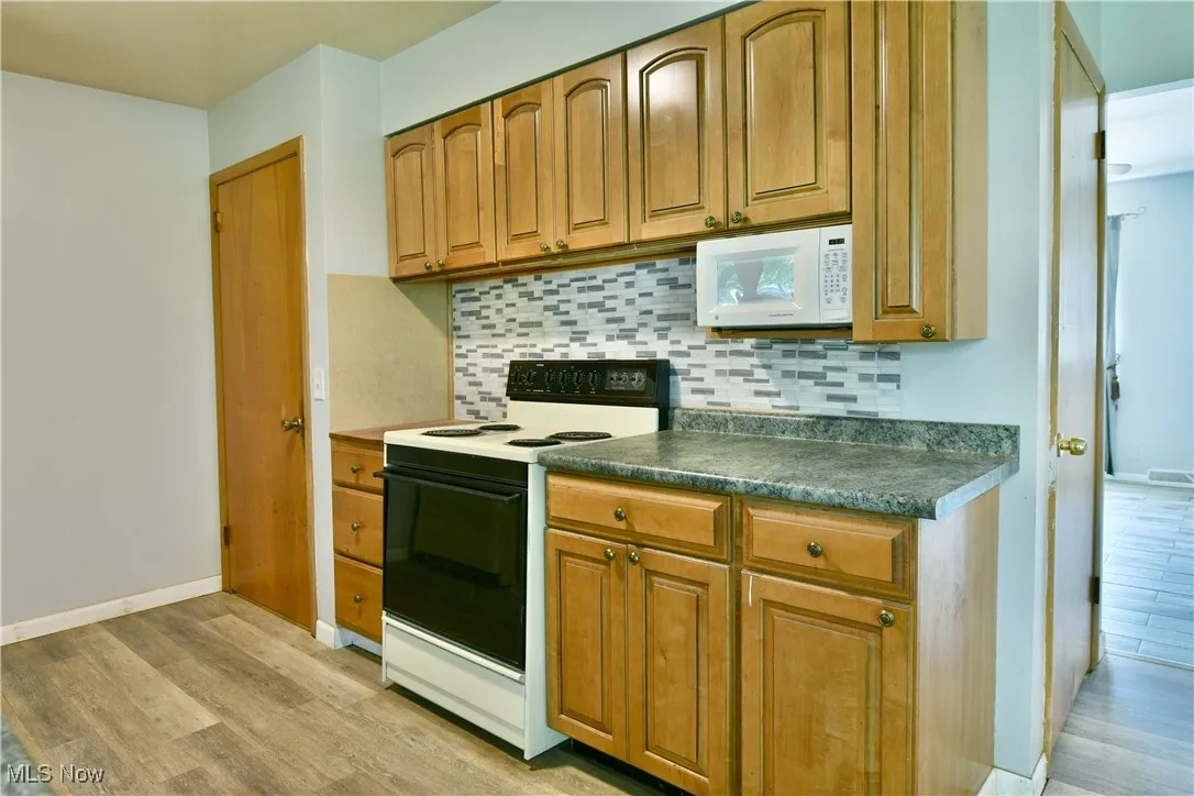 Kitchen with white appliances, light wood-style floors, backsplash, dark countertops, and brown cabinetry