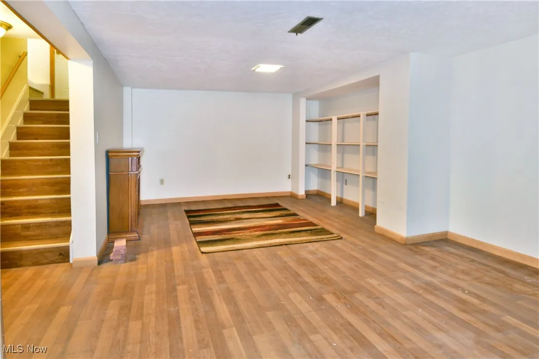 Finished below grade area with wood finished floors, stairway, and a textured ceiling