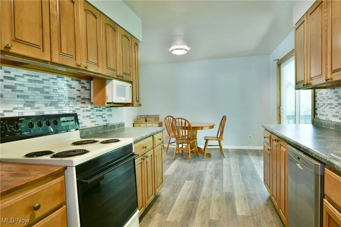 Kitchen featuring white appliances, light wood finished floors, backsplash, and brown cabinets