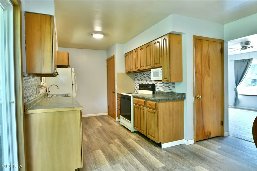 Kitchen with white appliances, light wood-style floors, backsplash, and brown cabinets