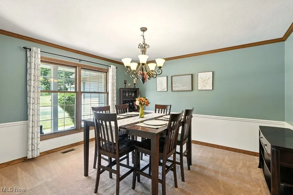Dining space featuring a chandelier, light colored carpet, and crown molding