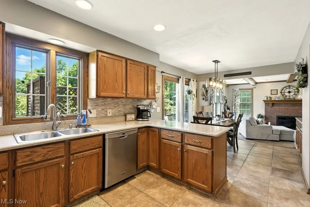 Kitchen with a peninsula, brown cabinetry, stainless steel dishwasher, light countertops, and decorative light fixtures