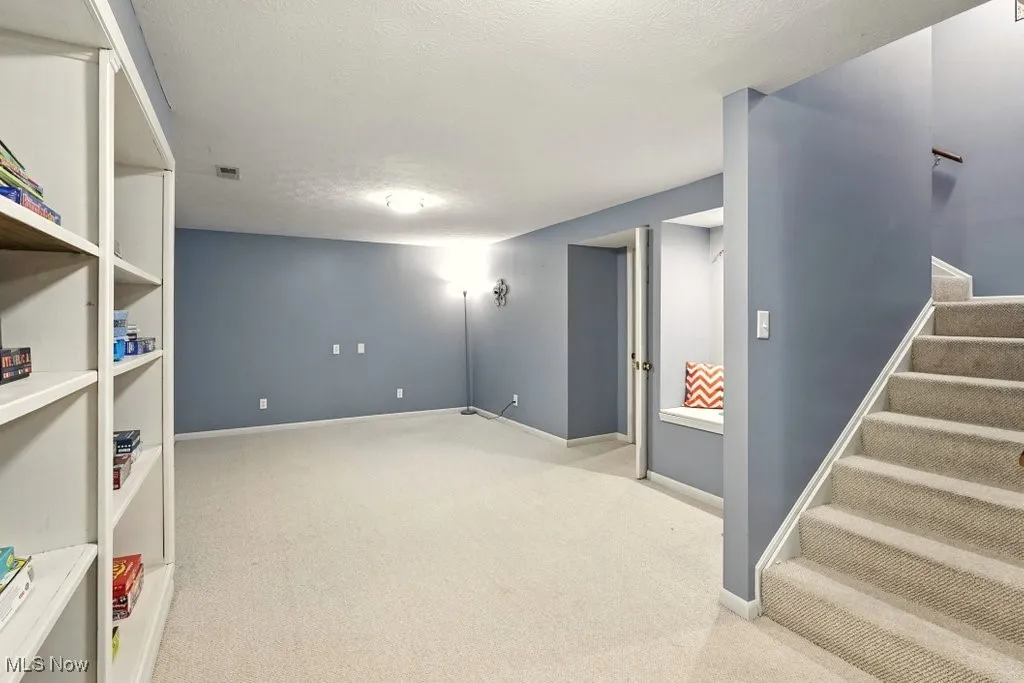 Finished basement featuring carpet floors, a textured ceiling, and stairs