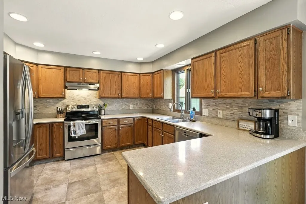 Kitchen featuring stainless steel appliances, brown cabinetry, a peninsula, light countertops, and recessed lighting