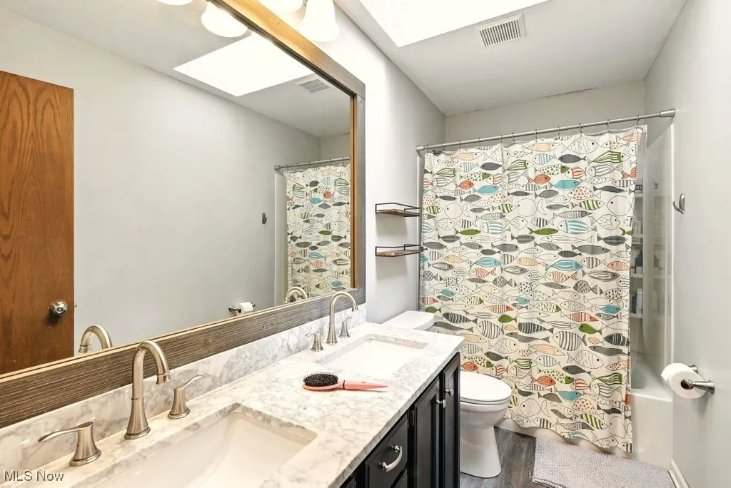Bathroom with double vanity, a skylight, shower / bathtub combination with curtain, and wood finished floors