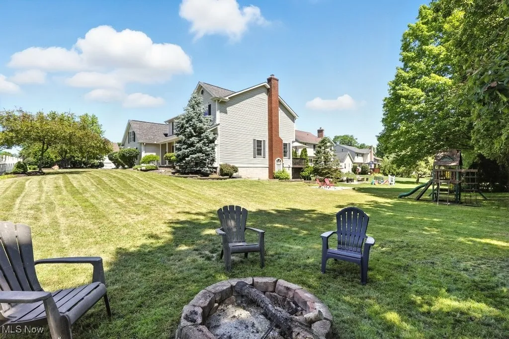 View of grassy yard featuring a fire pit and a playground